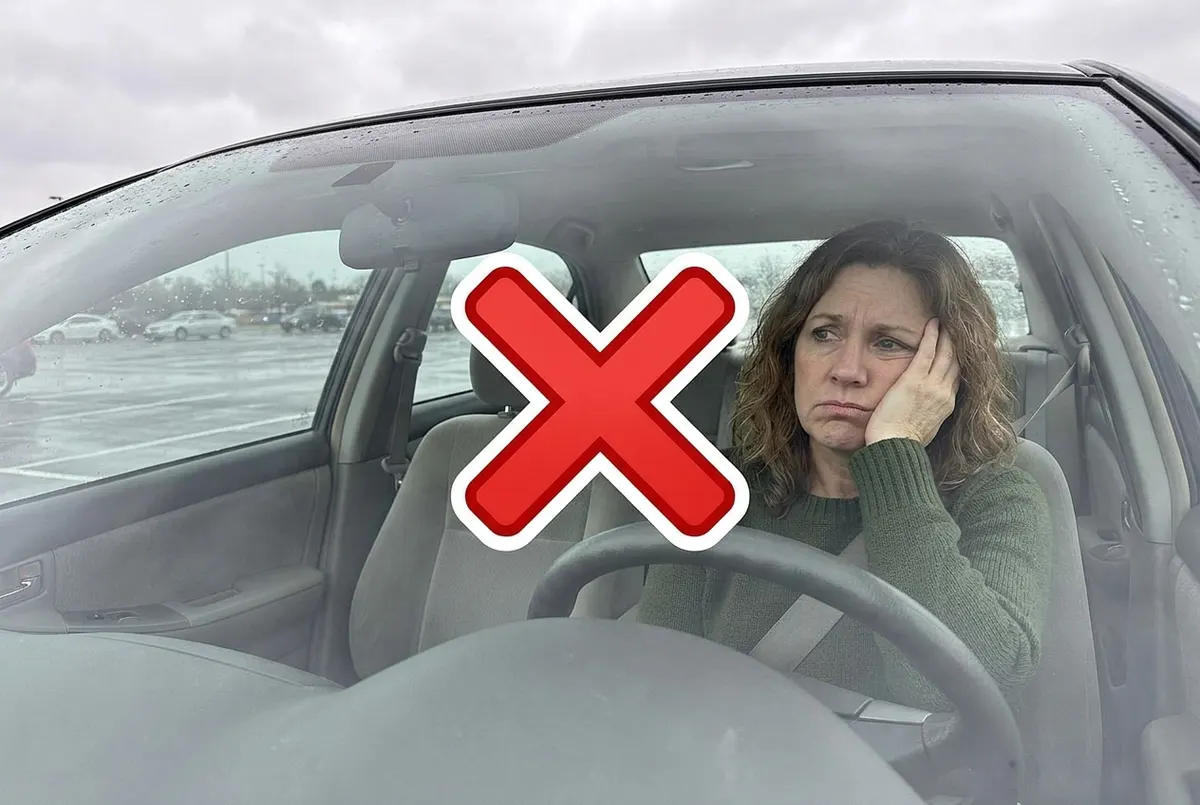 A woman, 35–54, sitting alone in a parked car, hand resting on her cheek in quiet frustration, staring through the windshi...