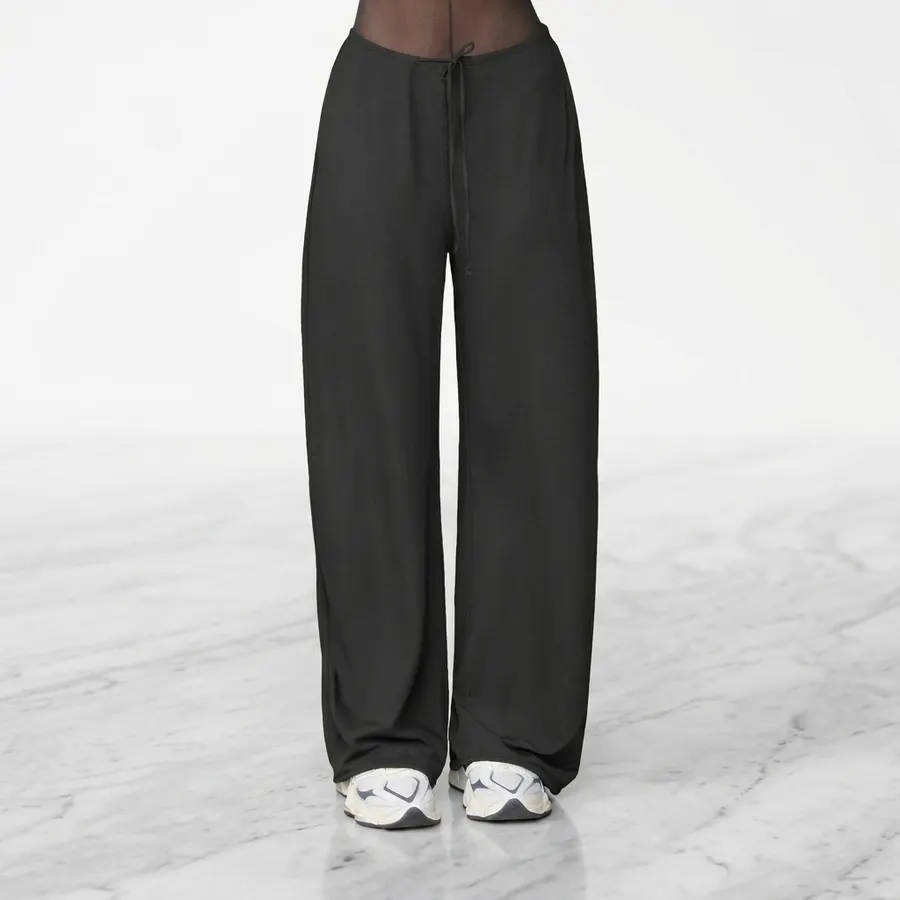 A pair of neutral-toned casual pants folded neatly on a light wood surface, morning sunlight casting clean diagonal shadow...