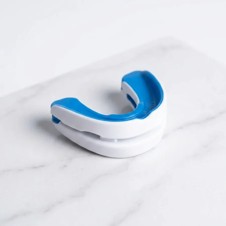 A close-up of an adjustable anti-snoring mouthpiece resting on a soft white surface in clean morning light, photographed f...