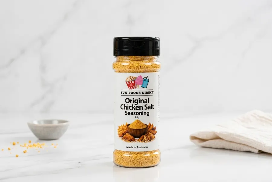 A modern seasoning shaker bottle standing upright on a clean marble kitchen countertop beside a wooden spoon and small cer...