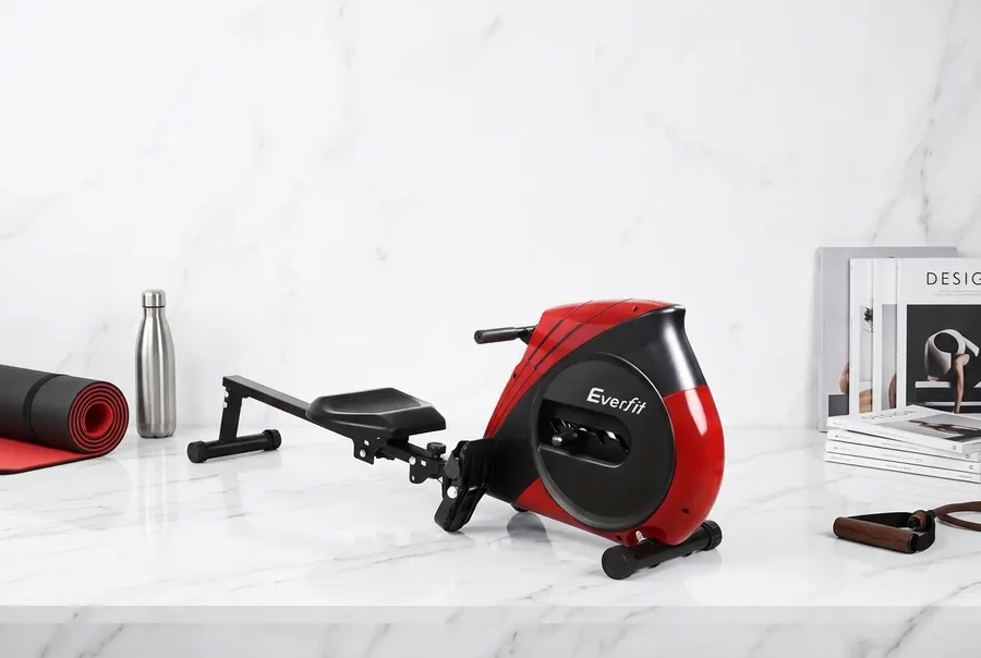 A sleek modern rowing machine in matte black with a clean minimalist design, positioned at a slight angle on a light hardw...