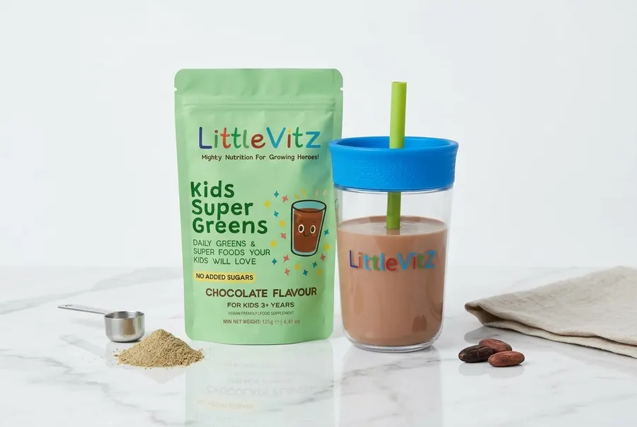A matte chocolate-brown pouch of children's greens powder stands upright on a clean white kitchen counter, occupying 60% o...