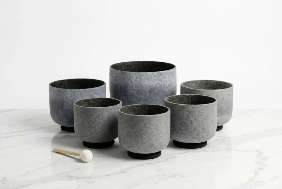 A single frosted white quartz singing bowl rests centered on a dark wooden meditation bench, occupying roughly 60% of the ...