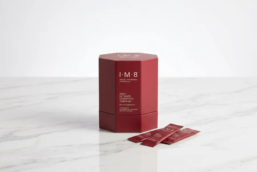 A sleek canister of daily greens supplement centered upright on a white marble surface with morning sunlight casting clean...