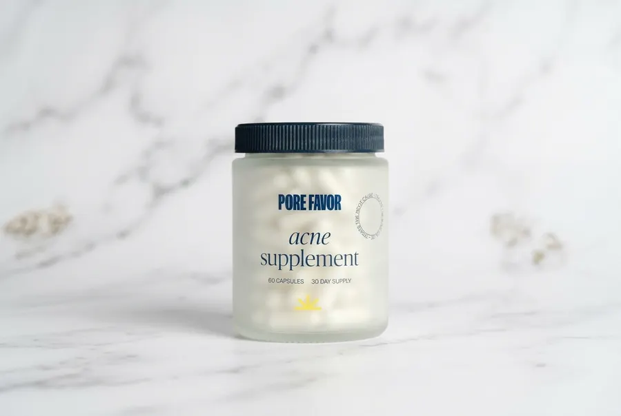 A matte black bottle of daily acne supplement capsules on a clean white marble bathroom counter, soft natural window light...