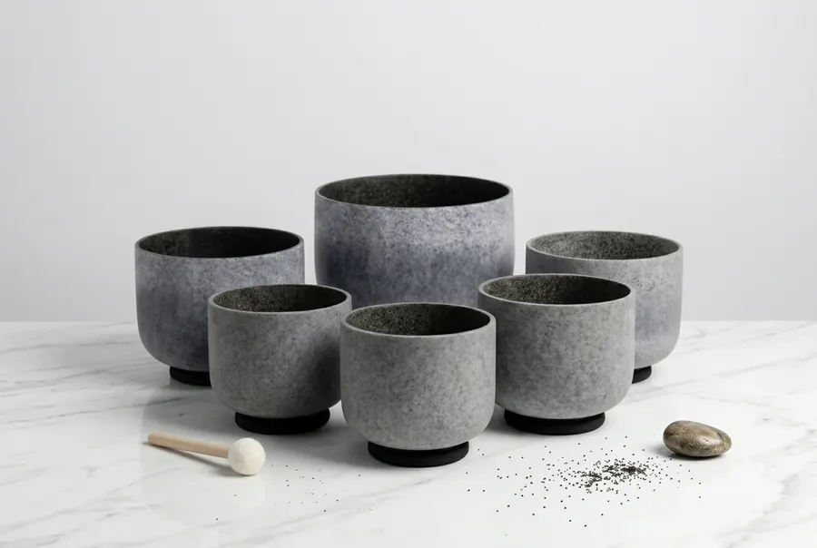 A complete set of seven black crystal singing bowls arranged in ascending size on a clean wooden surface, each bowl showin...