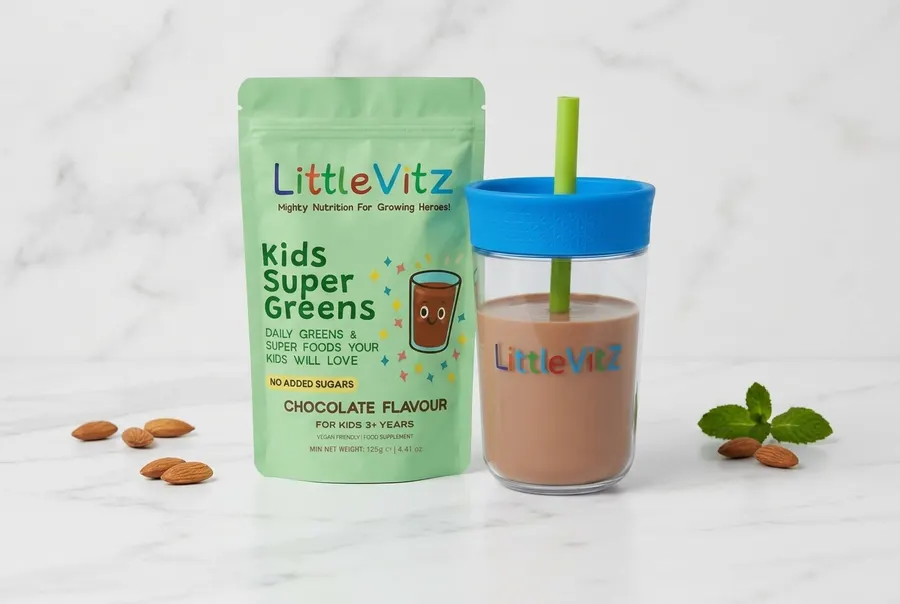 A jar of kids' chocolate-flavored greens powder centered on a light wooden surface, surrounded by fresh spinach leaves, a ...