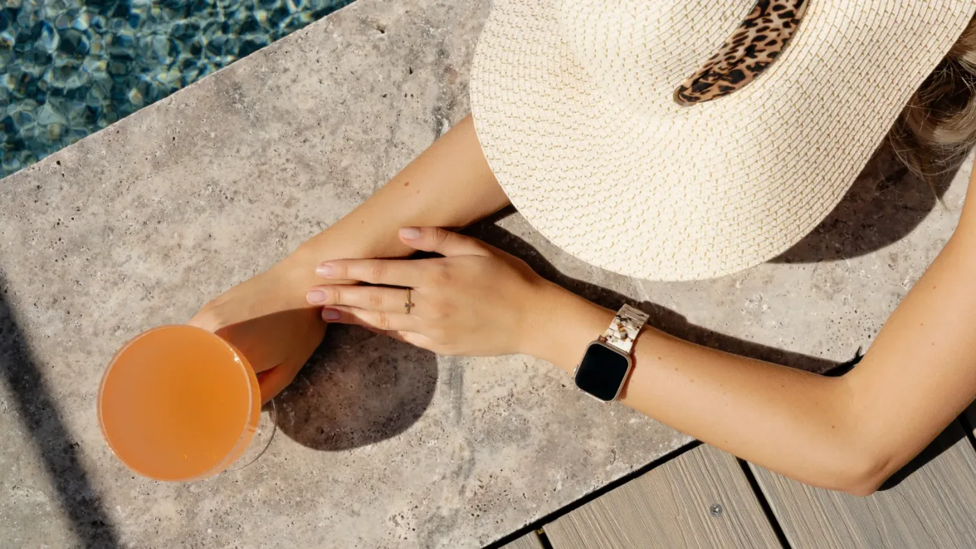 A woman aged 38 at her desk mid-afternoon, slumped slightly forward in her chair, rubbing her left wrist with her right ha...