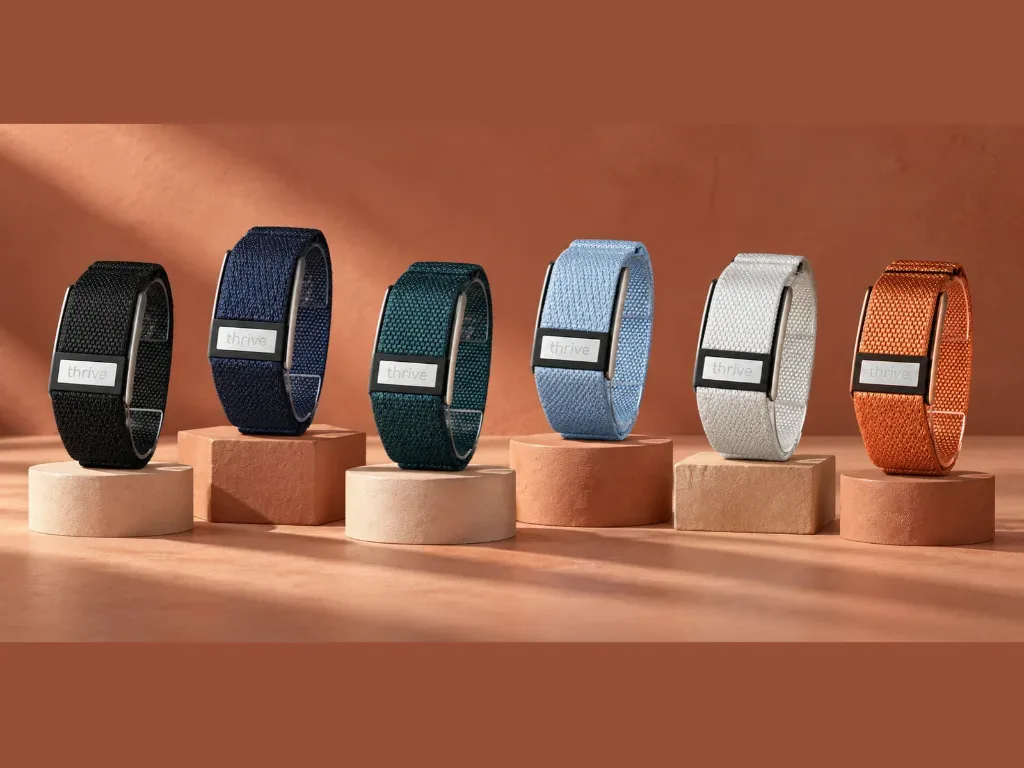 A slim screen-free wearable band in a woven textile finish resting on a smooth stone surface beside a folded linen napkin ...